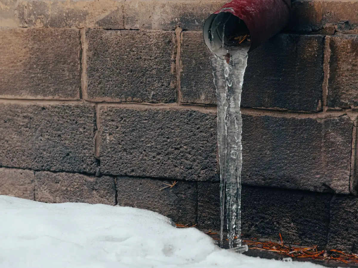 Ice forming on a dripping downspout above snow-covered ground