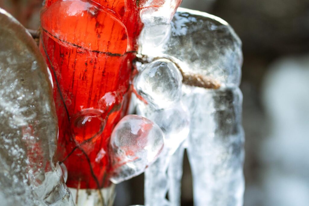 Red pipe encased in thick ice during a winter freeze