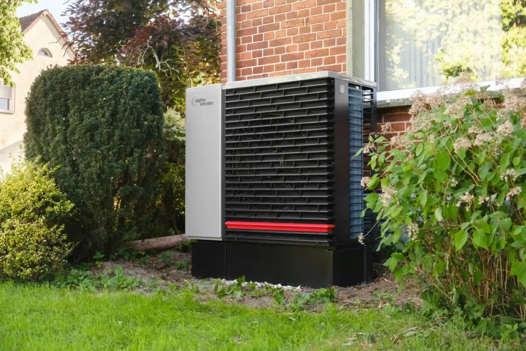 Modern outdoor heat pump unit beside a brick house and garden