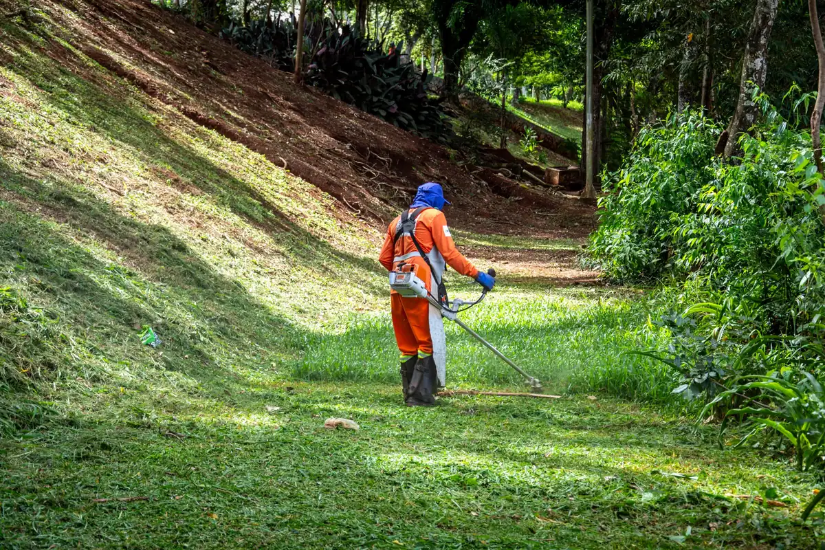 Landscaper in safety gear mowing a steep green hillside