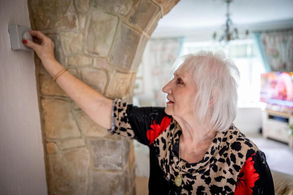 Homeowner adjusting a wall thermostat in her living room as the weather turns cold