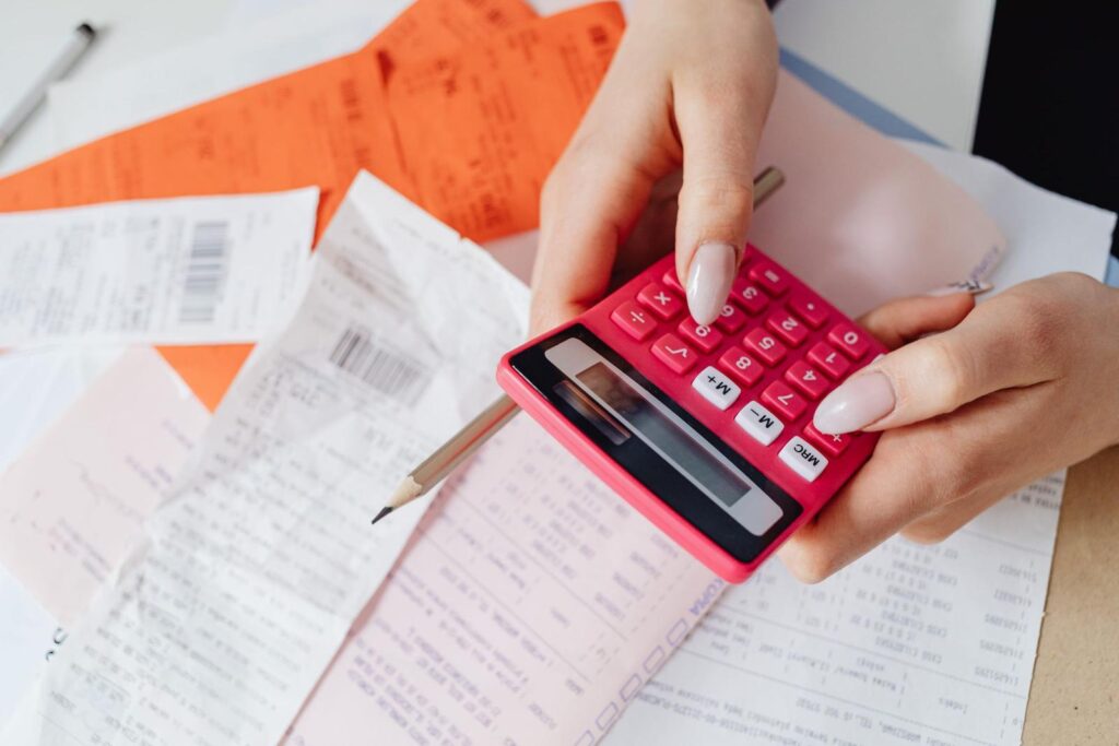 Hands using a red calculator over a pile of invoices and receipts