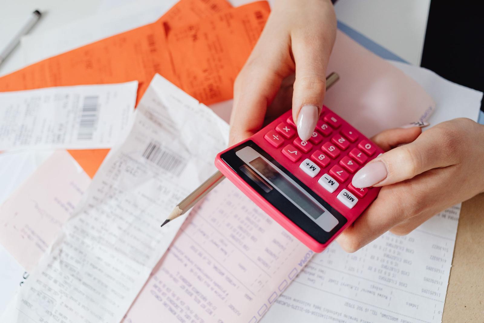 Hands using a red calculator over a pile of invoices and receipts