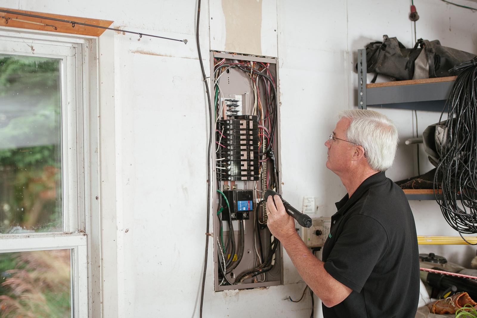 Electrician inspecting a residential breaker panel mounted on a garage wall