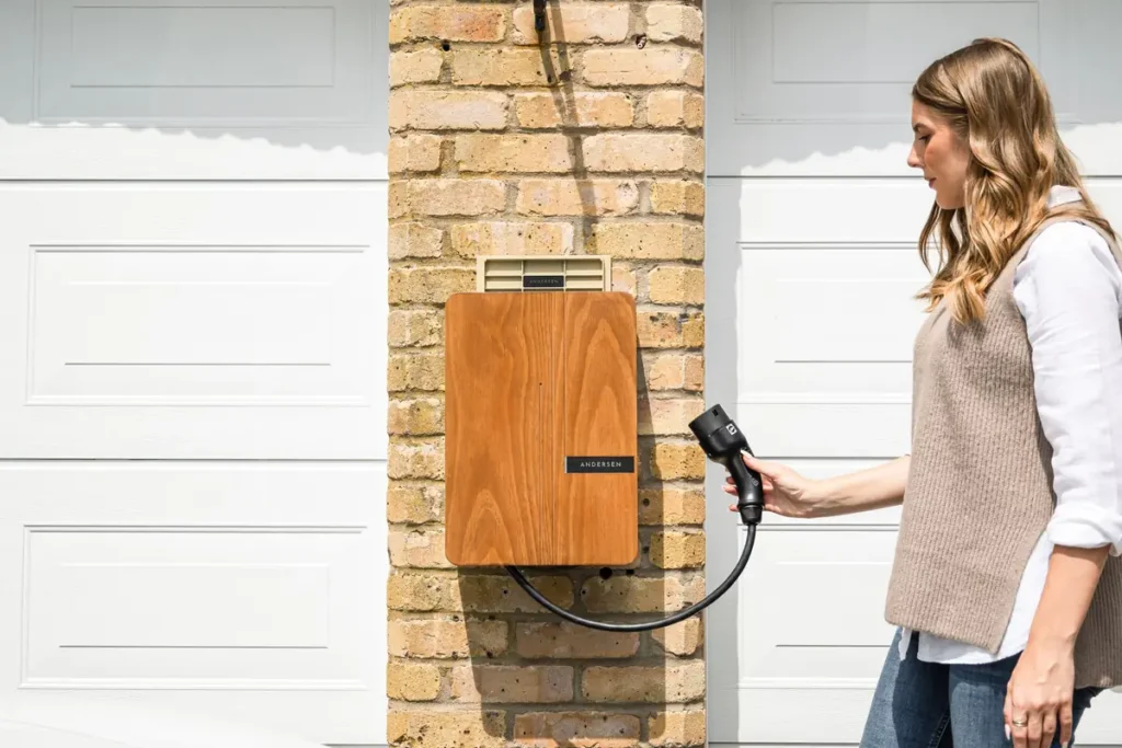 Woman plugging a charging cable into a wall-mounted home EV charger next to a garage door