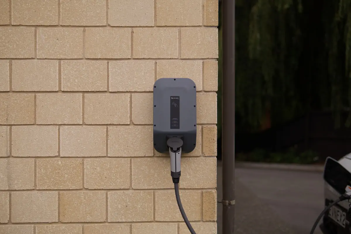 Wall-mounted electric vehicle charger with its cable plugged in against a tan brick wall