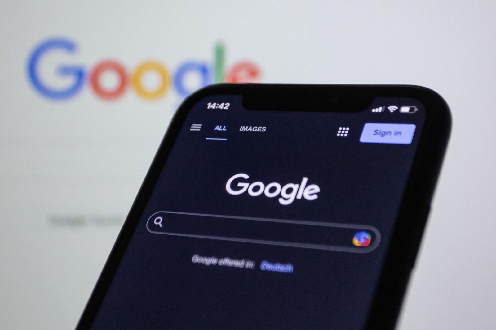 Smartphone showing the Google search bar in front of a laptop screen with the Google logo
