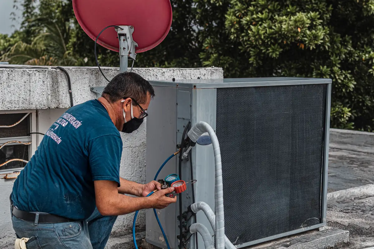 HVAC technician in a face mask connecting gauges to an outdoor air conditioning unit