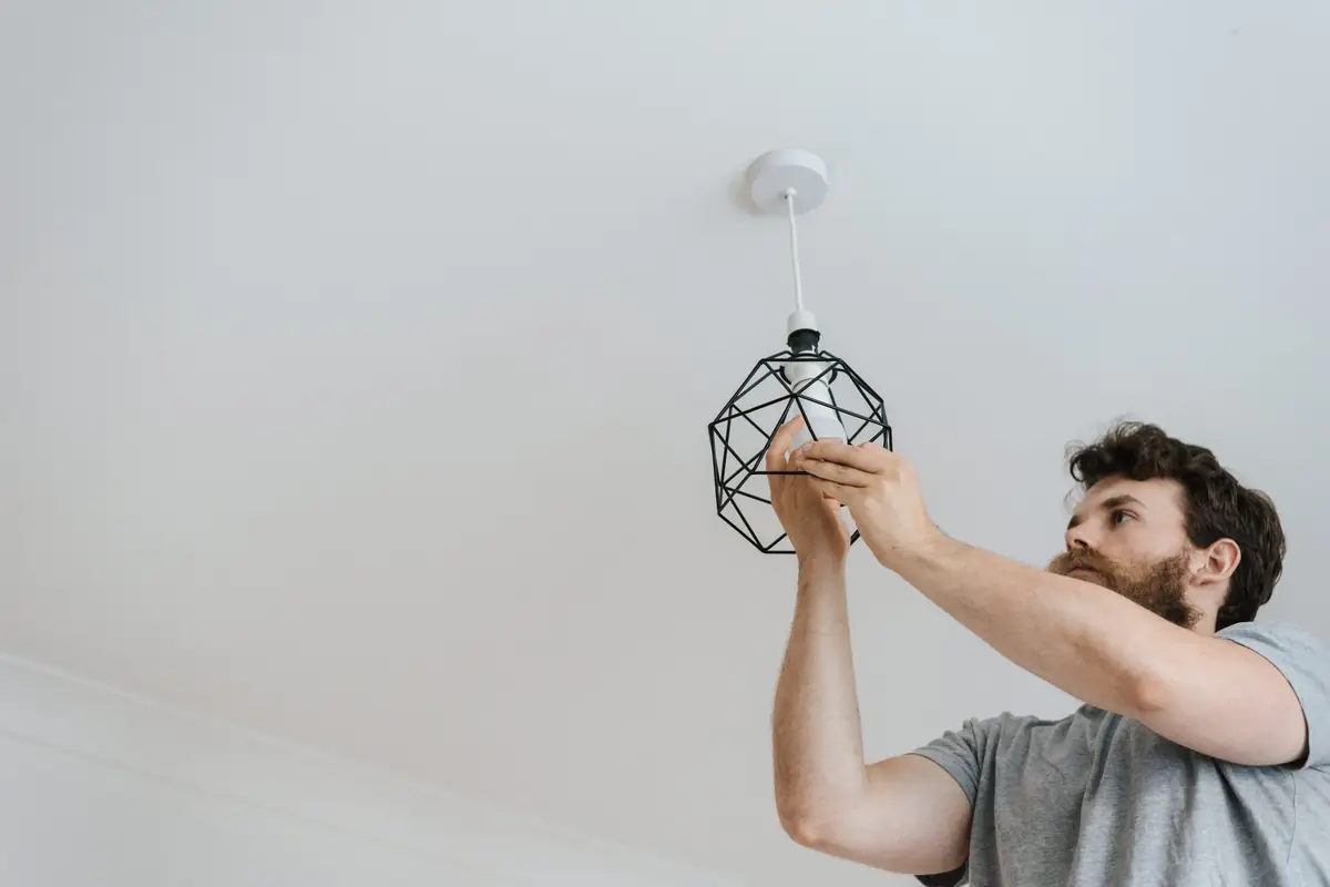 Electrician installing a geometric pendant light fixture on a white ceiling