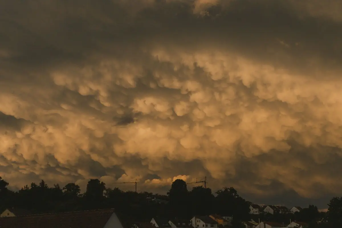 Dramatic storm clouds lit orange at dusk over a line of rooftops