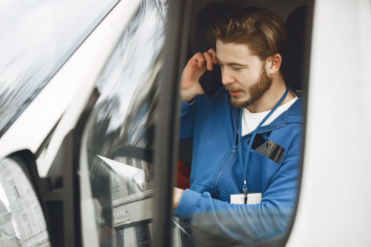 Service technician in a blue jacket answering a phone call from the driver's seat of a work van