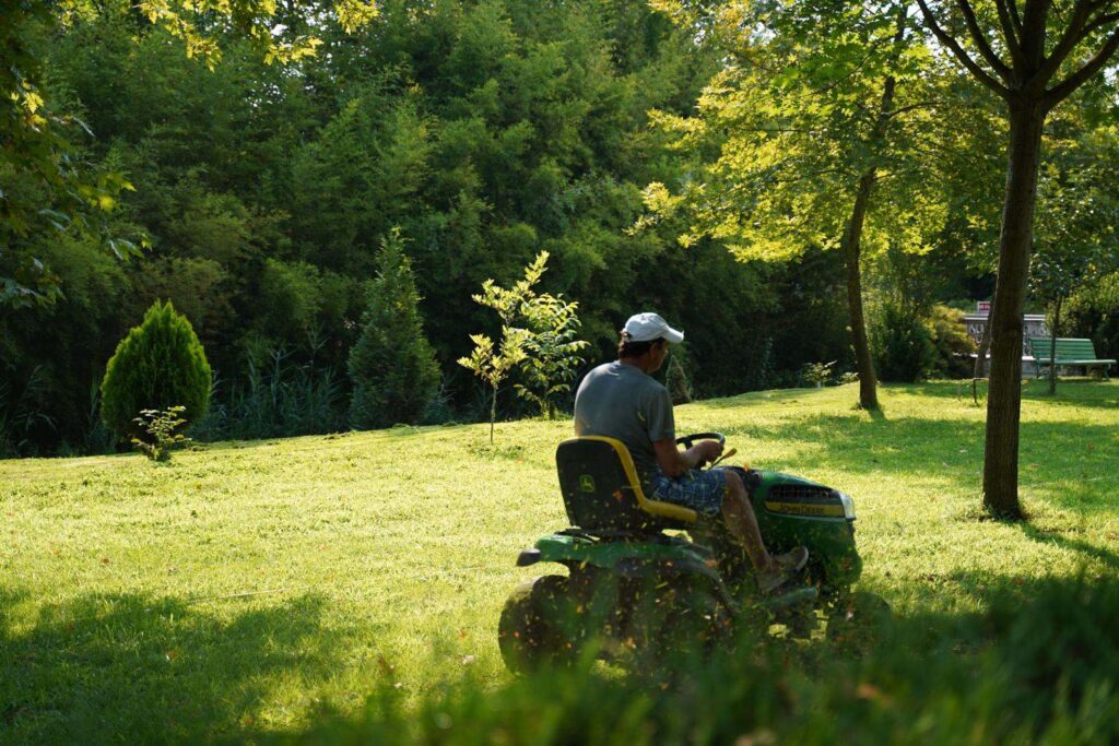 Landscaper on a riding mower cutting a large green lawn on a sunny day